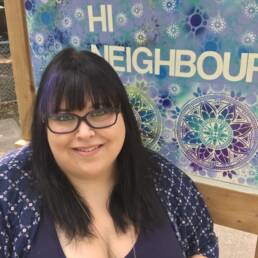 portrait of Jennifer Gordon in front of a sign that says Hi Neighbour