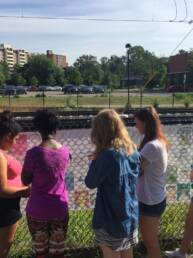 group of 5 youth looking at a wall of outdoor art portraits