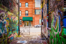 Ally with graffiti in brick walls and a unique key shaped fence at the end